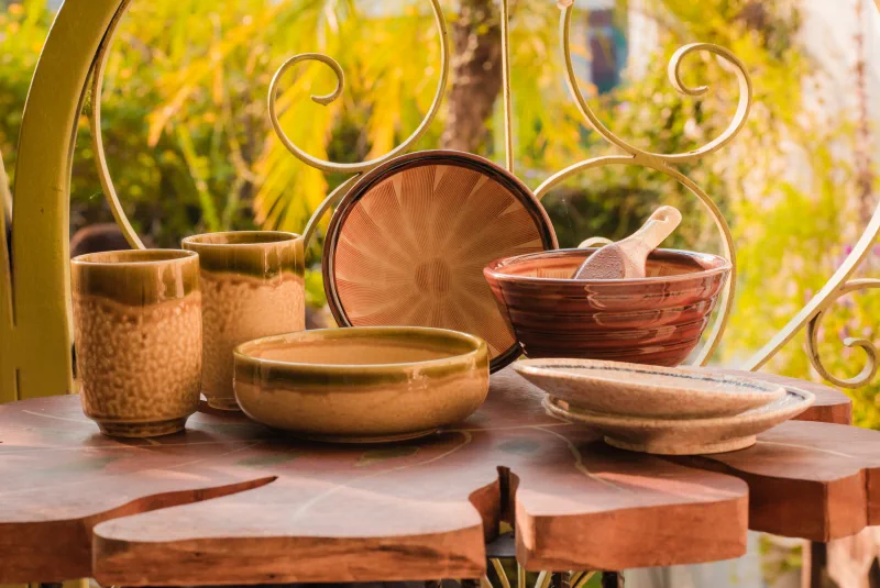 A complete ceramic table set of textured cups, bowls, spoon and speckled plates arranged in warm garden light