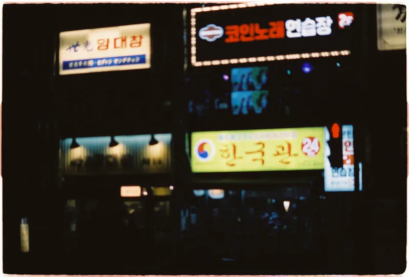 Layers of softly focused illuminated restaurant signs fill a dark Seoul facade