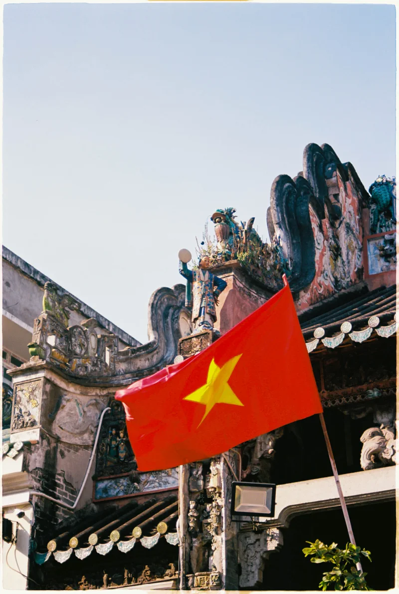 A bright Vietnamese flag crosses the sculpted roofline of an old Sài Gòn temple