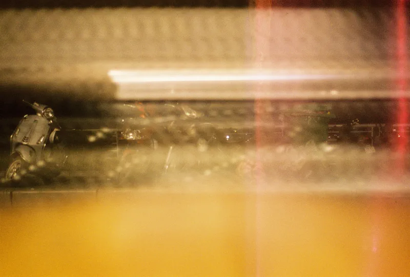 A silver scooter appears through amber motion blur, reflections and a vertical red light leak