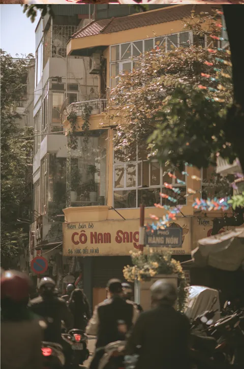 A sunlit Hàng Nón street in Hà Nội seen through moving motorbike traffic