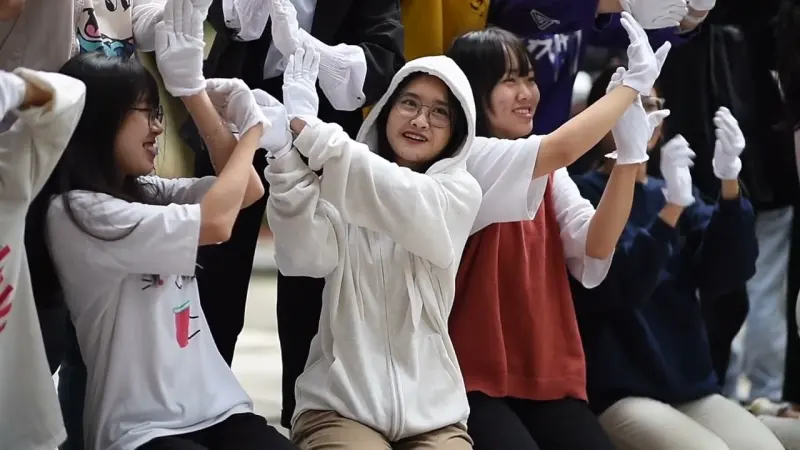 Dancers in white gloves rehearse a raised-hand routine, laughing between counts